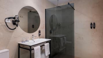 Un baño moderno con ducha de vidrio, espejo redondo y tocador con lavamanos y barra para toallas.