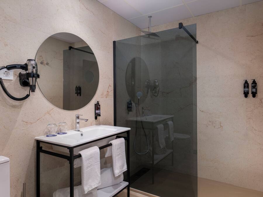 A modern bathroom with a glass-enclosed shower, a round mirror, and a vanity with a sink and towel rack.