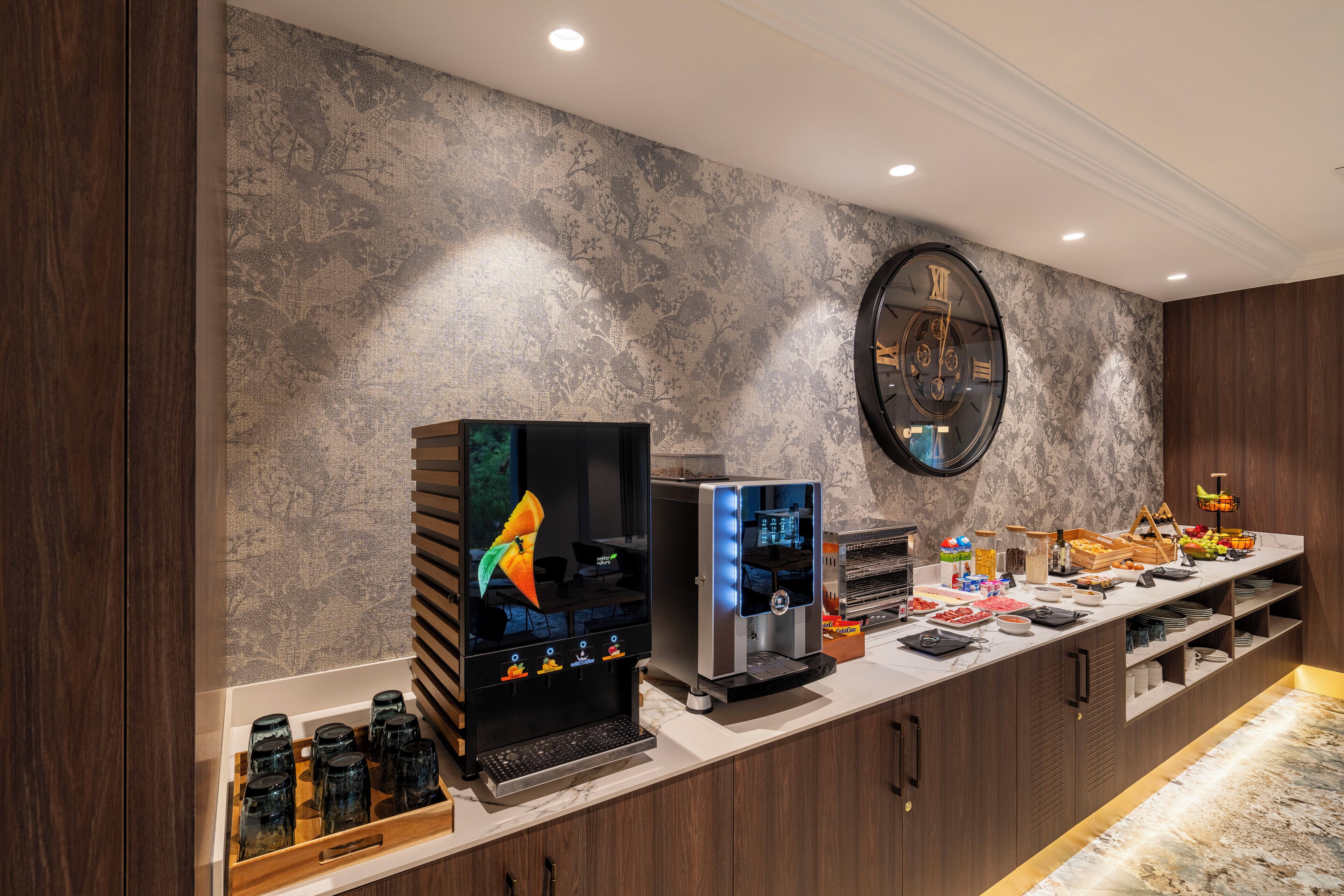 A modern kitchen with a coffee station, a large clock, and a marble countertop.