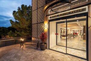 The exterior of Hotel Molina Plaza with a modern facade, a seating area with a bench and potted plant, and a view into the lobby area.