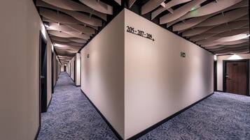 Un pasillo de hotel con diseño moderno, que destaca por una estructura de techo original y un suelo alfombrado.