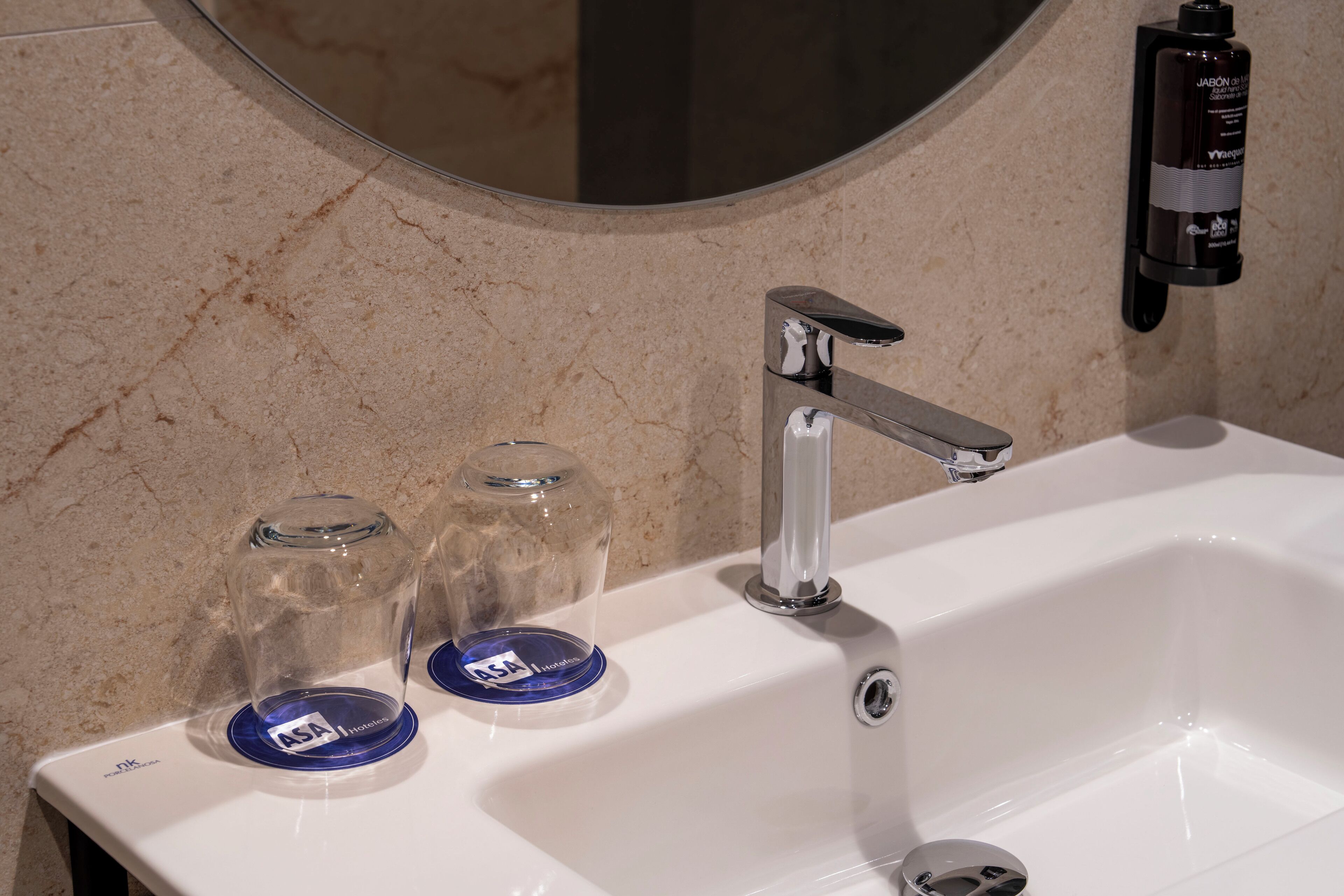 A bathroom sink with a chrome faucet, a mirror above it, and two clear glass jars with blue lids on the sink.