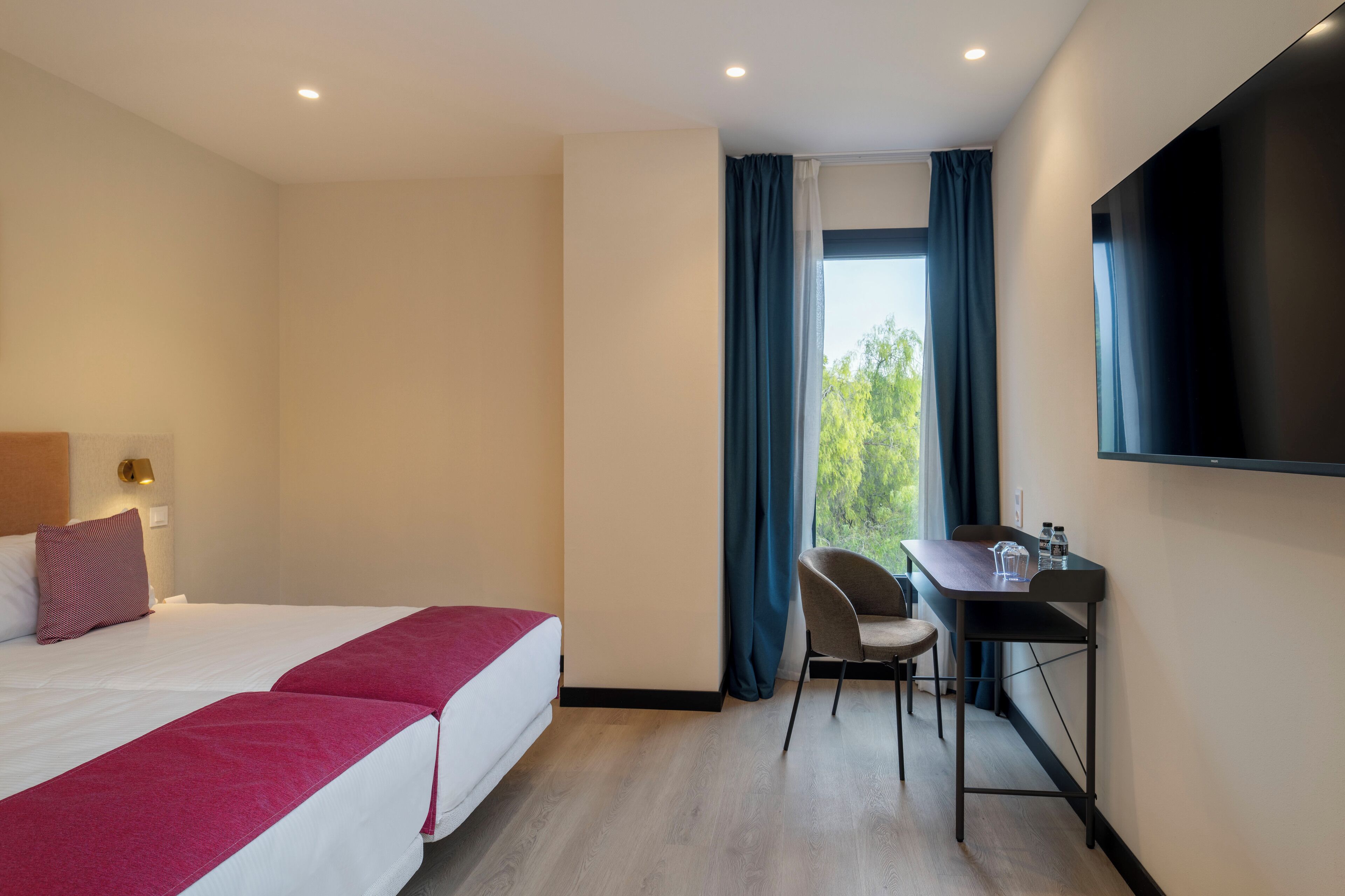 Een hotelkamer met twee bedden, een bureau, een stoel, een televisie en een raam met gordijnen.