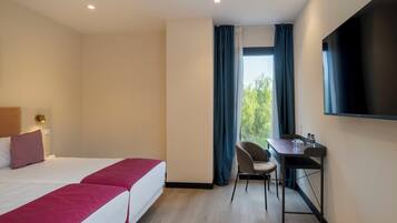 Quarto de hotel com duas camas, uma escrivaninha, uma cadeira, uma televisão e uma janela com cortinas.