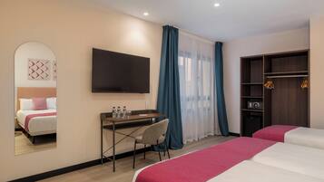 A hotel room with two beds, a desk with a chair, a TV mounted on the wall, a wardrobe, and a mirror reflecting the bed.