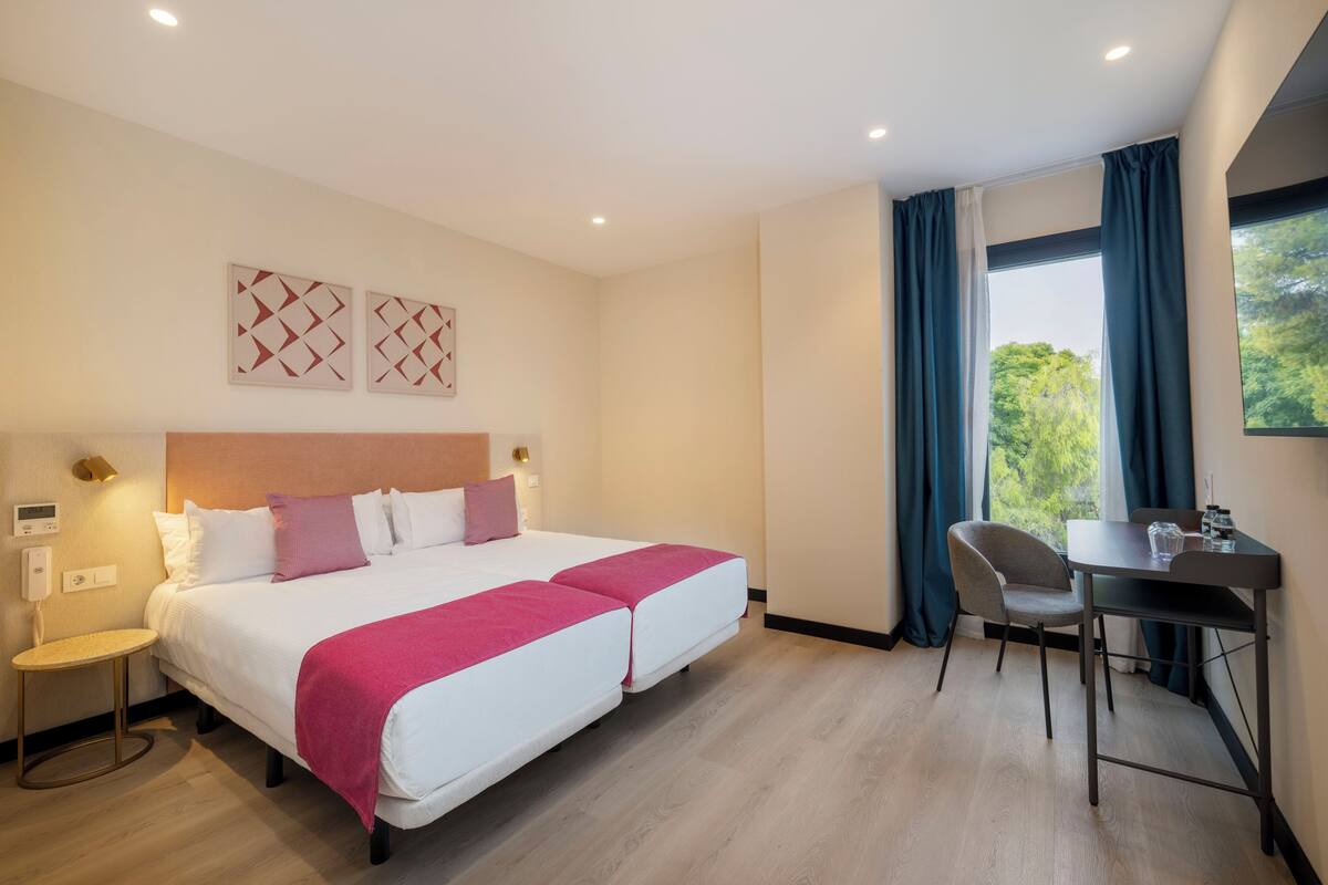 Une chambre d’hôtel avec un lit double, un bureau avec une chaise et une vue sur la verdure par la fenêtre.