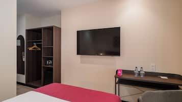 A hotel room with a bed, a TV mounted on the wall, a desk with a chair, and a wardrobe.