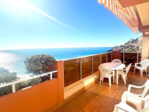 A balcony with a view of the sea, a table with chairs, and a tiled floor.
