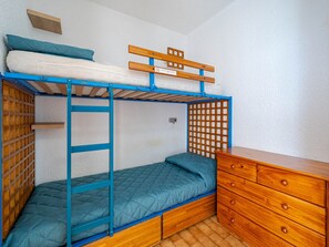 Uma cama beliche com escada de madeira e estrutura azul, um aparador de madeira e uma pequena prateleira.