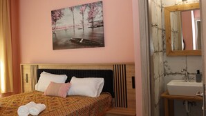 Ein Schlafzimmer mit Bett, Nachttisch und einem Badezimmer inklusive Waschbecken und Spiegel.