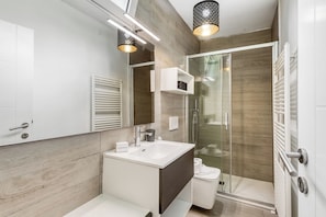 A modern bathroom with a white sink, dark cabinet, and a glass shower enclosure. - Secret Of Lugano With Lake View (Lugano)