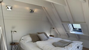 A modern bedroom with a sloped ceiling, a large bed, bedside tables, a floor lamp, and a window with a view. - 1 bedroom accommodation in Callantsoog (Callantsoog)