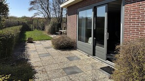 A modern building with a brick facade, large sliding glass doors, and a gravel pathway leading to a seating area. - 1 bedroom accommodation in Callantsoog (Callantsoog)