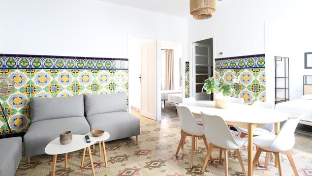 Una sala de estar moderna con un sofá gris, una mesa de comedor redonda con sillas blancas y baldosas de suelo estampadas.