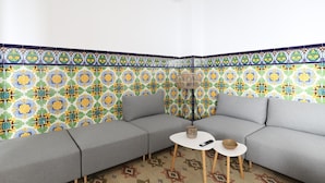 Habitación de esquina con un sofá gris, dos mesas blancas y una pared de baldosas estampadas.