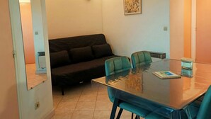 A room with a glass table, two chairs, a sofa, and a wall-mounted light fixture. - Canet-en-Roussillon: Cozy 1-Bedroom with AC and Parking, Steps from the Beach! (Canet-en-Roussillon)