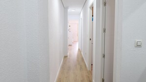 Un pasillo estrecho con paredes blancas y piso de madera, que conduce a una habitación con una puerta.