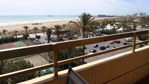 Vista desde un balcón sobre una playa, con un estacionamiento y palmeras.