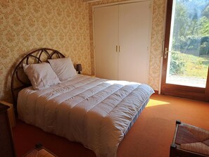 A bedroom with a bed, a wardrobe, and a view of greenery outside.