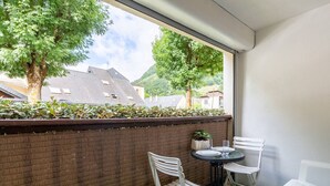 En balkon med murstensvæg, to hvide plastikstole, et lille rundt bord og en plantepotte.