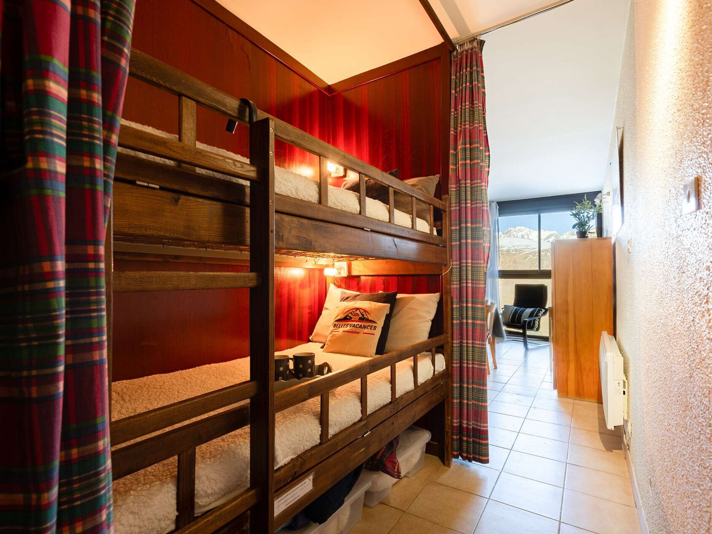 Une chambre avec des lits superposés, un mur rouge, un bureau en bois et une vue sur les montagnes.