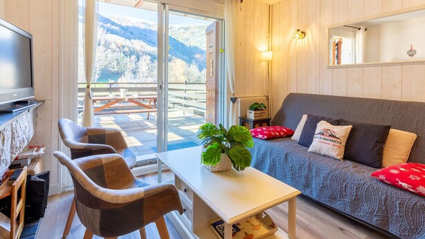 Una sala de estar moderna con un sofá, sillas, un televisor y vistas a montañas a través de puertas de cristal amplias.