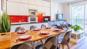 Una cocina moderna con armarios blancos, un salpicadero rojo y un comedor con una mesa de madera dispuesta para seis comensales.