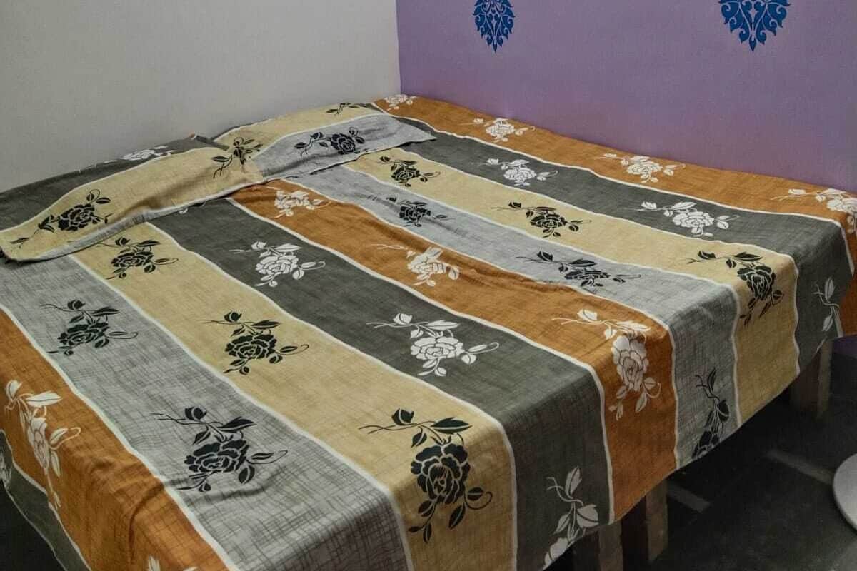 A single bed in a room with a purple wall and a patterned bedspread.