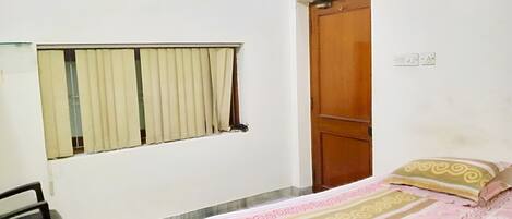 A small, simple room with a bed, a desk, and a window with curtains.