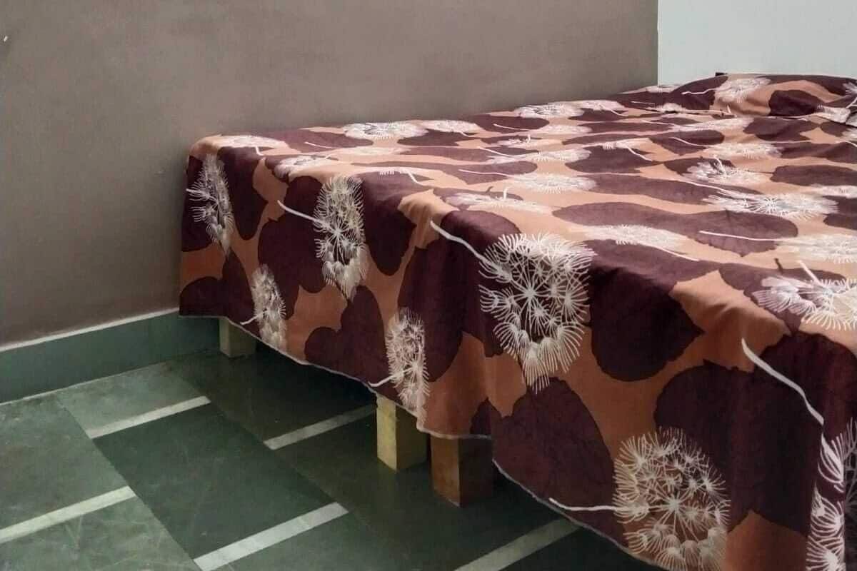 A room with a bed covered in a patterned bedspread, a green tiled floor, and a wall with a decorative pattern.