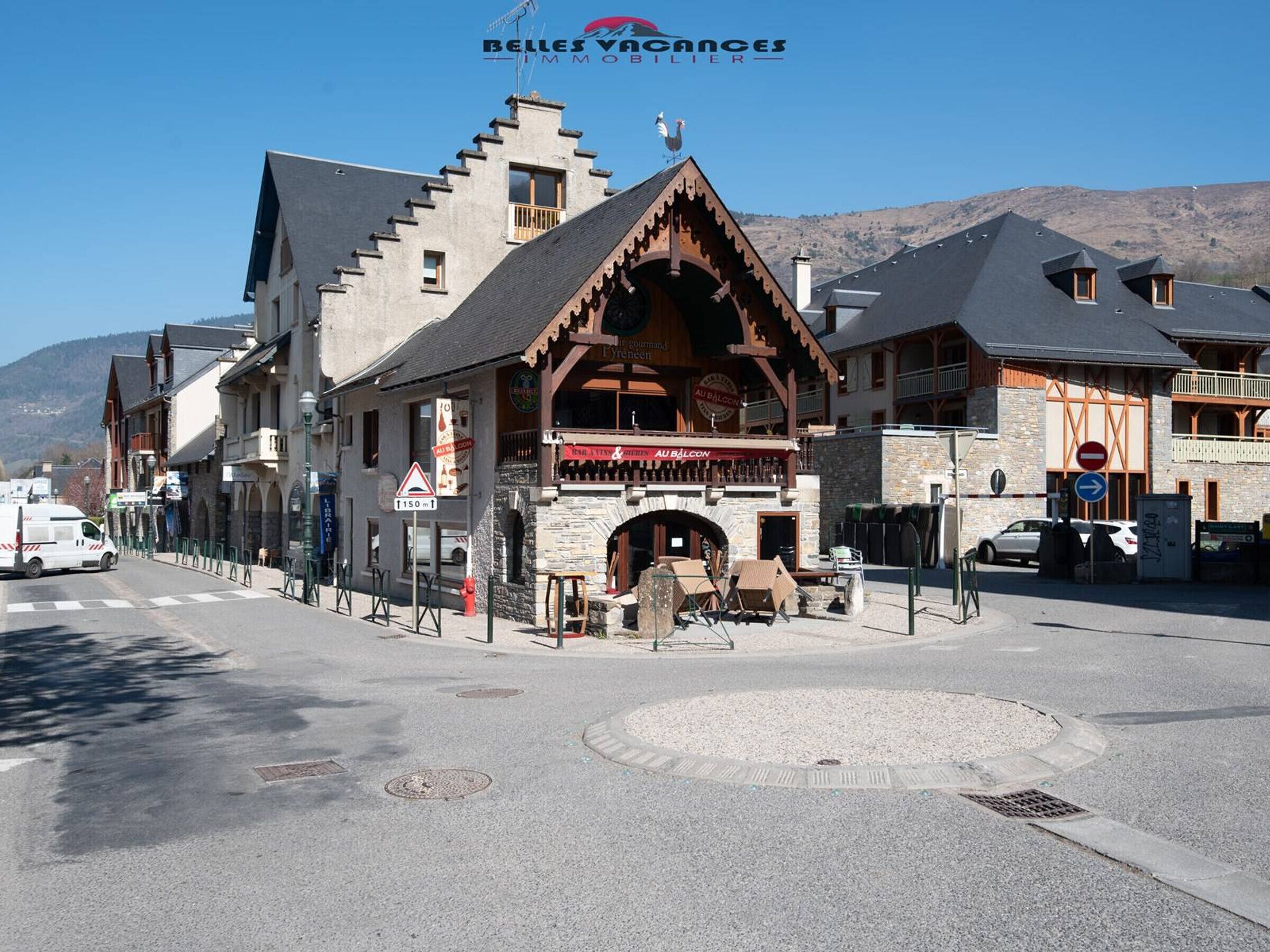 A traditional chalet-style building with a stone facade, wooden balconies, and a mountain backdrop.