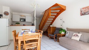 Una cocina moderna con armarios blancos, una mesa de comedor con sillas, una escalera, un sofá y una pequeña mesa con una planta.