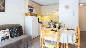 A compact living space with a kitchenette, a dining area with a table and chairs, and a sofa with decorative pillows. - Apartment for 4 near thermal baths and cable car in Saint Lary (Saint-Lary-Soulan)