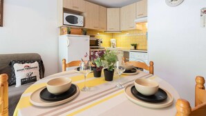 A compact kitchen with a microwave, stove, and dishwasher. There is a dining table with two bowls and a wine glass. - Apartment for 4 near thermal baths and cable car in Saint Lary (Saint-Lary-Soulan)