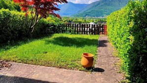 A paved pathway leading through a garden with a red tree and a large pot on the side.