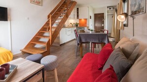 A cozy living room with a wooden staircase, a dining area, and a kitchen in the background.