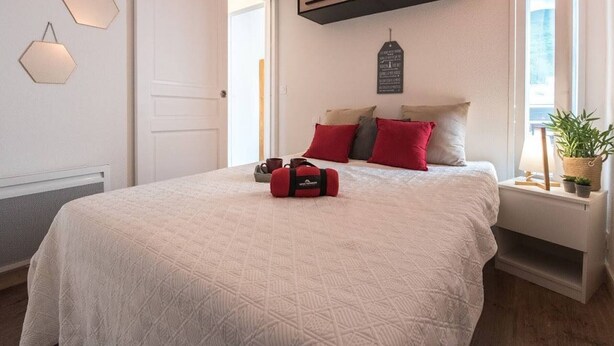 A bedroom with a large bed, a bedside table, a wall-mounted shelf, and a window with a view.