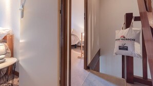 Ein Hotelzimmer mit einer Holztreppe, einem Bett mit beiger Bettdecke, einer weißen Wand und einer Tasche, die an der Wand hängt.