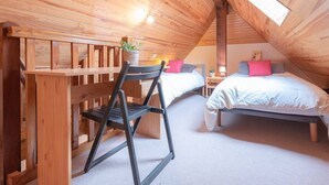 Ein gemütliches Schlafzimmer im Dachgeschoss mit Holzbalken, einem Holztisch, zwei Betten und einem Stuhl.