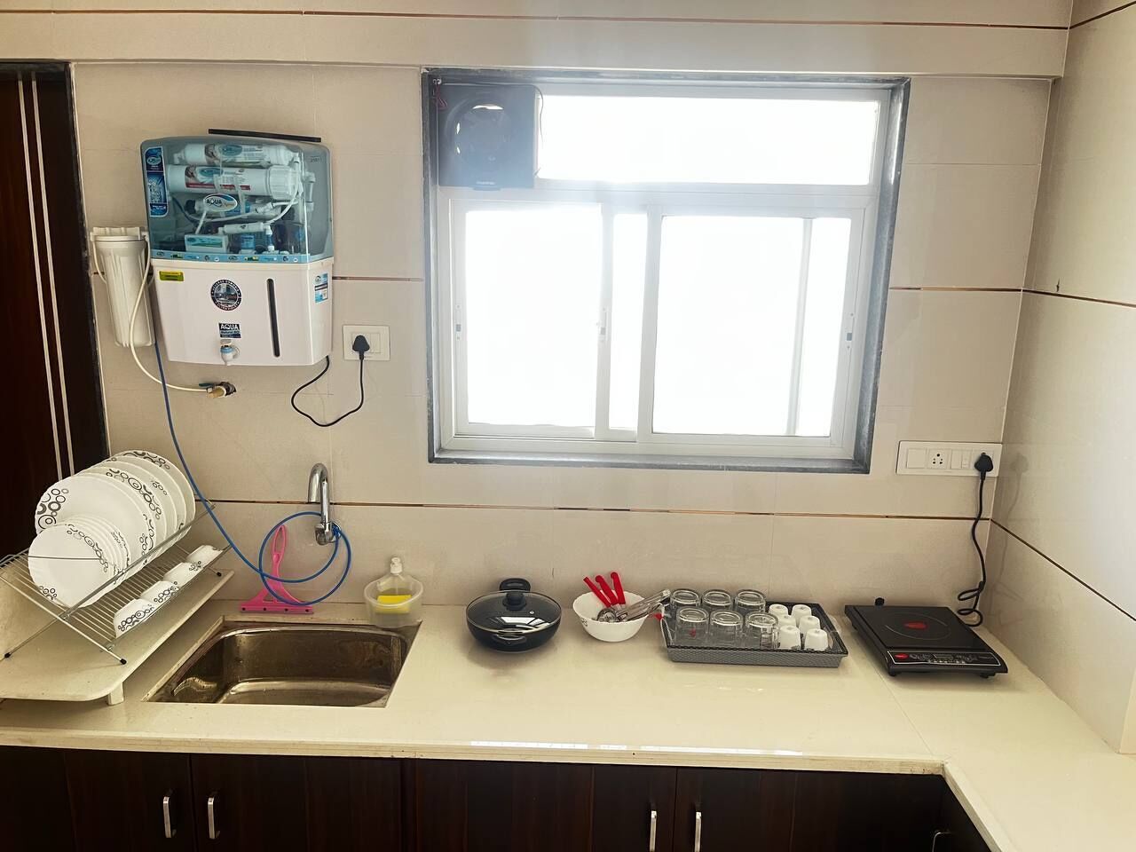 Una cocina con un escurreplatos, una ventana, dispensador de agua, un lavamanos, estufa y un refrigerador pequeño.