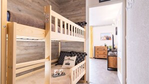 Ein Schlafraum mit Etagenbetten, Holzboden, Schreibtisch mit Stuhl und einem kleinen Schrank.