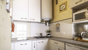 Eine kompakte Küche mit weißen Schränken, einer eingebauten Mikrowelle, einer Kaffeemaschine und einem kleinen Spülbecken.
