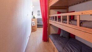 Una habitación pequeña con literas, un rincón de descanso y una cortina.