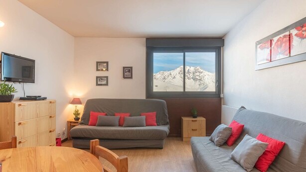 Una sala acogedora con un sofá gris, una mesa de comedor de madera y un televisor montado en la pared.