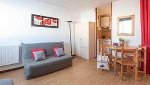 Una sala moderna con un sofá gris, una mesa de comedor con sillas, una cortina roja y una cocina al fondo.