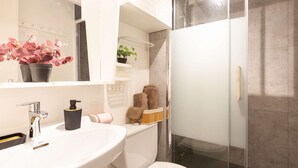 A modern bathroom with a white sink, a mirror, a glass shower enclosure, and a toilet.