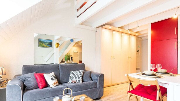 A modern living room with a grey sofa, a wooden coffee table, and a red dining chair.