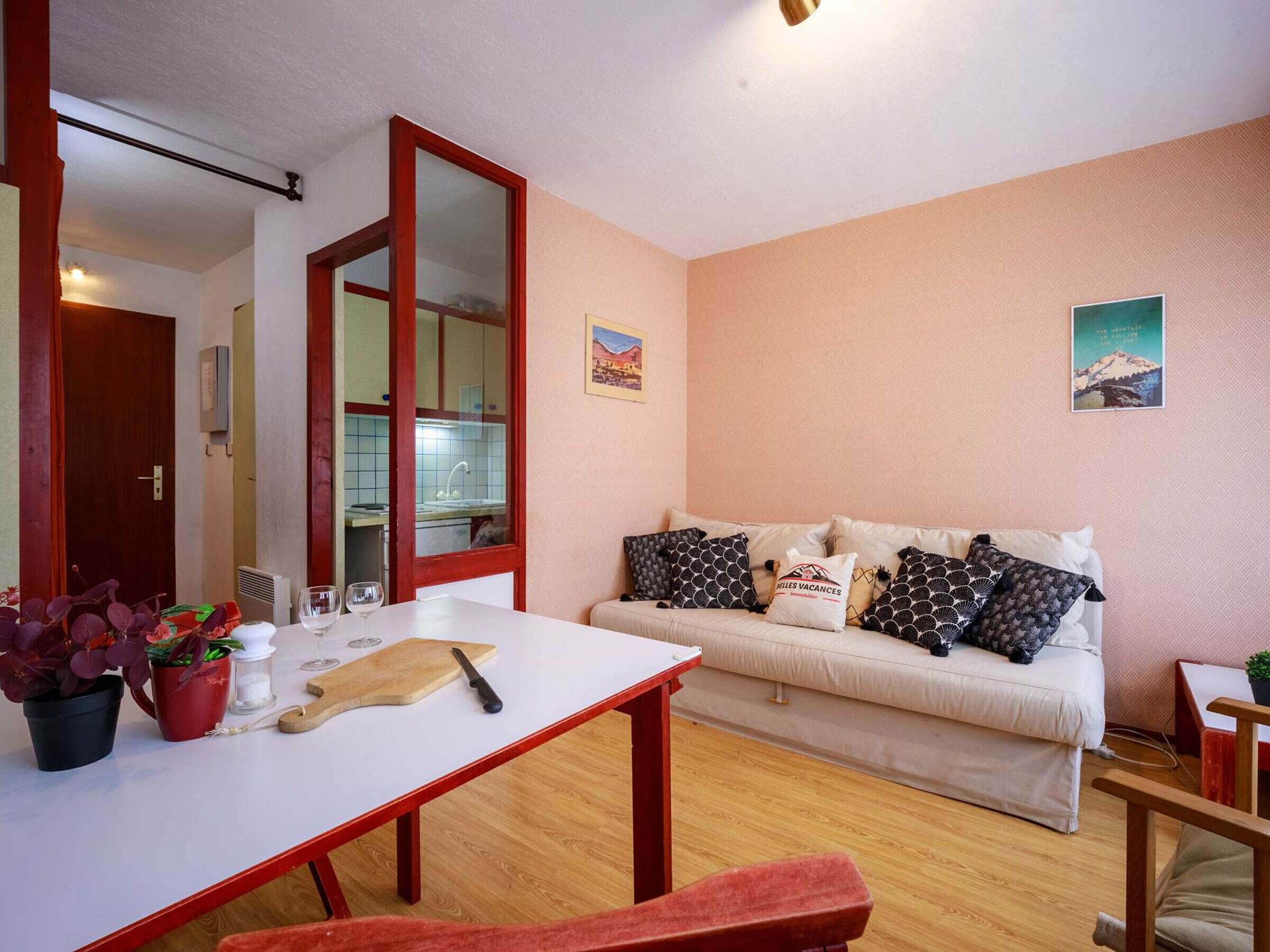 Ein gemütliches Wohnzimmer mit einer Couch, einem Esstisch und einem durch eine Glastür einsehbarer Küchenbereich.