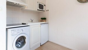 A compact kitchen with white cabinetry, a built-in microwave, a washing machine, and a small potted plant on the counter.