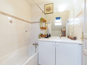 Ein Badezimmer mit Badewanne, Waschbecken und Spiegel. Die Wände sind mit dekorativen Fliesen versehen und es gibt eine hängende Pflanze.